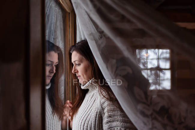 Приваблива жінка дивиться крізь вікно за мереживом куратан . — стокове фото
