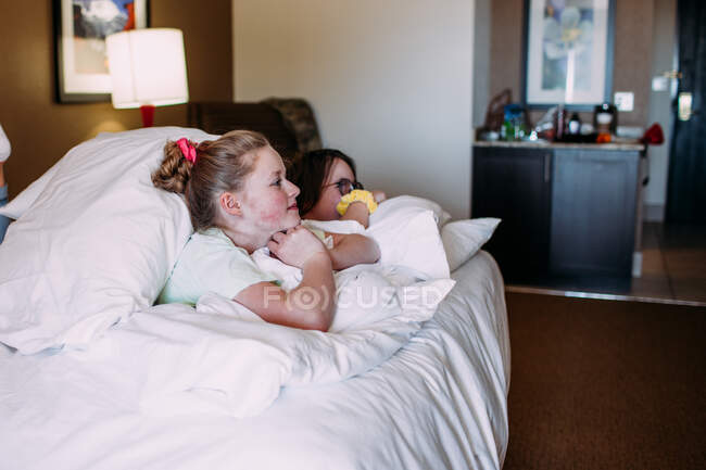 Two happy young girls relaxing on a bed in a hotel room — Stock Photo
