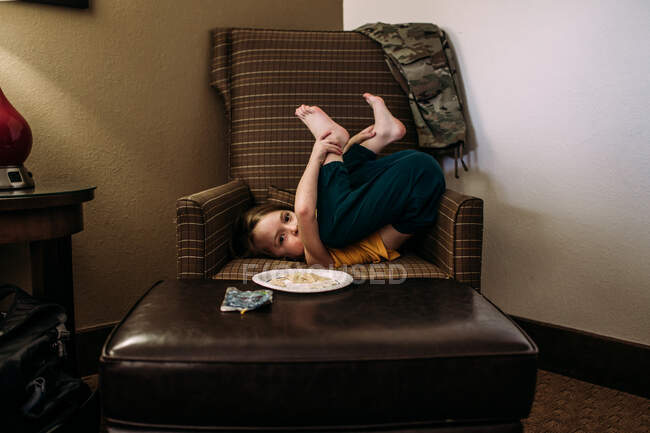 Маленький ребенок, лежащий на стуле в глупой позе — стоковое фото