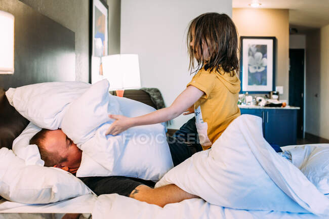 Happy young child playing with father on a bed in a hotel room — Stock Photo