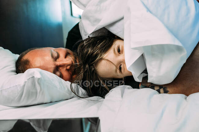 Heureux papa et jeune enfant se blottissant sur un lit souriant — Photo de stock