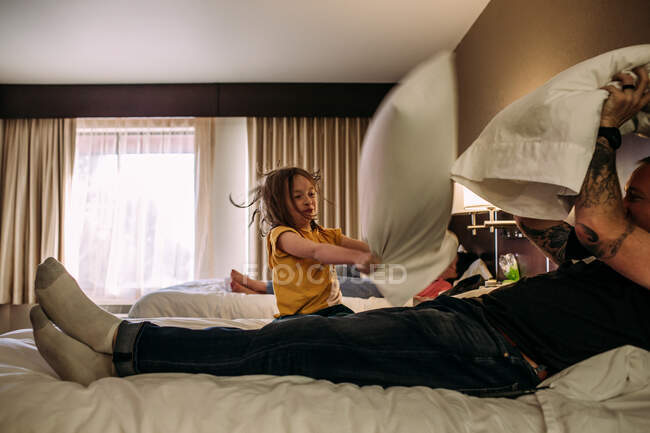 Giovane ragazza e papà avendo una lotta cuscino in una camera d'albergo — Foto stock