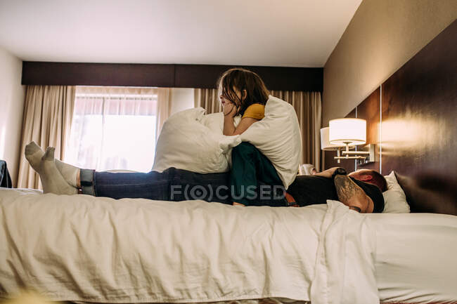 Criança sentada em cima do pai assistindo TV em um quarto de hotel — Fotografia de Stock