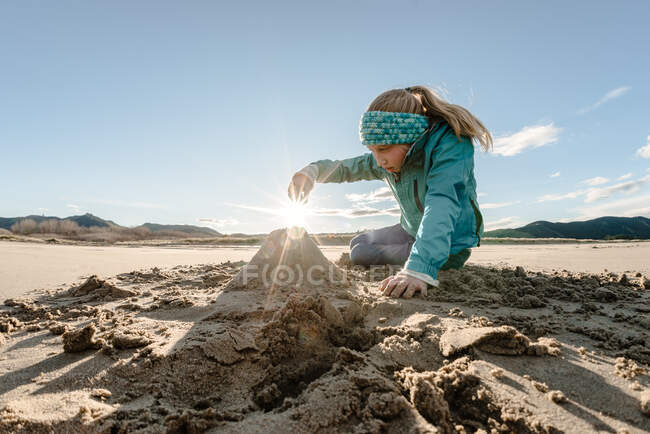 Blonde haired girl playing in sand on sunny cold day at beach — Stock Photo