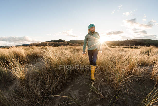 Счастливая девушка в куртке и сапогах, гуляющая по траве в солнечный вечер — стоковое фото