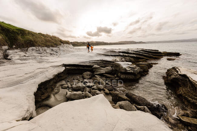 Pai e criança caminhando na costa rochosa perto do oceano na Nova Zelândia — Fotografia de Stock