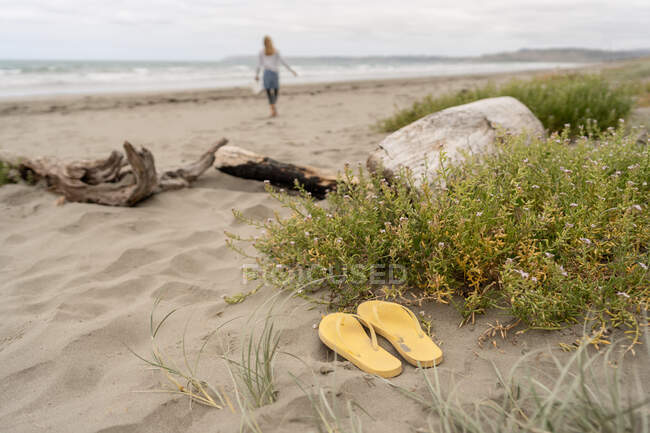 Tongs jaunes jandales dans le sable avec enfant en arrière-plan en Nouvelle-Zélande — Photo de stock