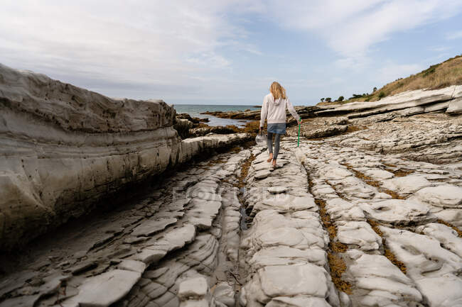 Menina com rede e balde andando sobre rochas perto do oceano na Nova Zelândia — Fotografia de Stock