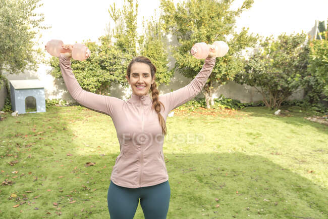 Молода жінка робить вправи з гантелями в парку — стокове фото