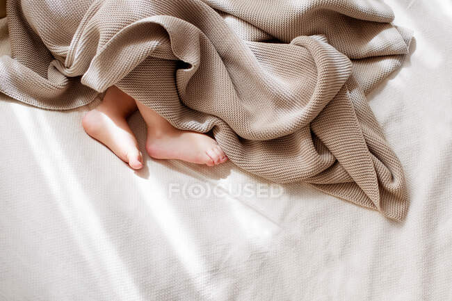Baby little feet covered with lightweight cotton baby knit blanket — Stock Photo