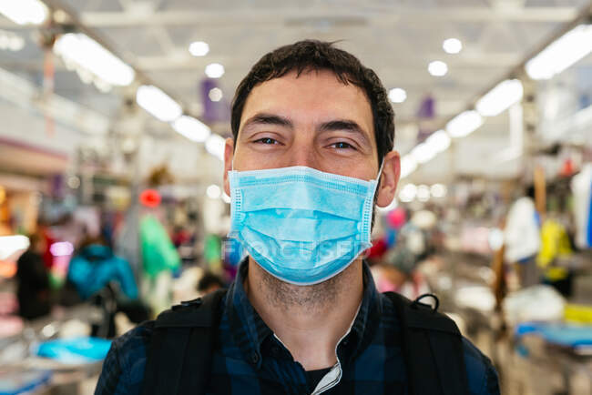 Jovem no mercado está usando uma máscara facial — Fotografia de Stock