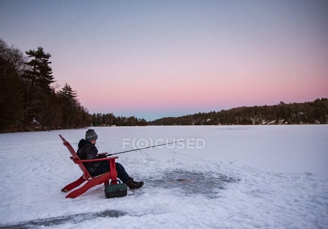 Menino pesca enquanto sentado na neve — Fotografia de Stock
