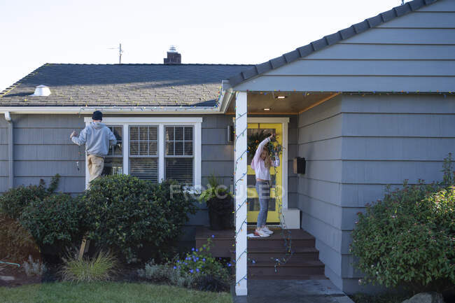 Uomo e ragazza che decorano una casa residenziale con luci per le vacanze — Foto stock