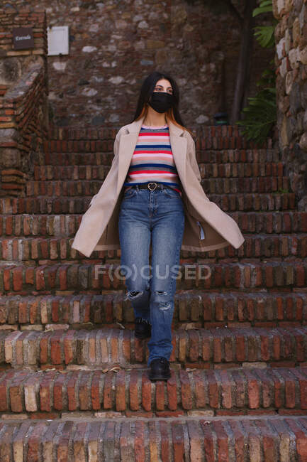 Natural young woman with mask descending the stairs of an old urban construction — Stock Photo