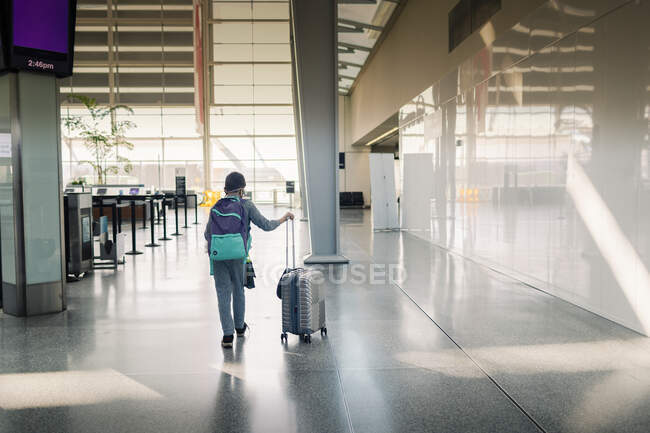 Back view pre-teen carrying backpack pulling suitcase airport terminal — Stock Photo