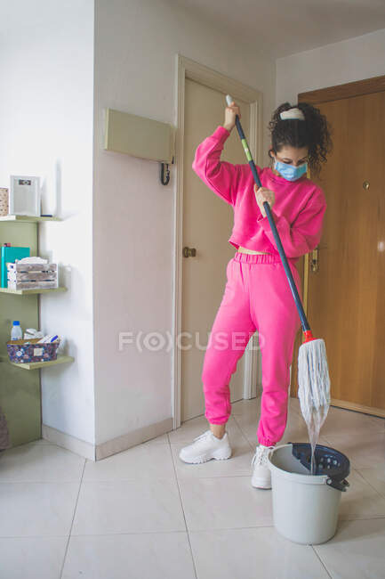 Mujer joven en máscara médica piso de limpieza - foto de stock