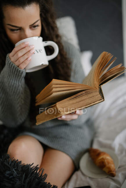 Mujer joven leyendo libro en el sofá en el dormitorio - foto de stock