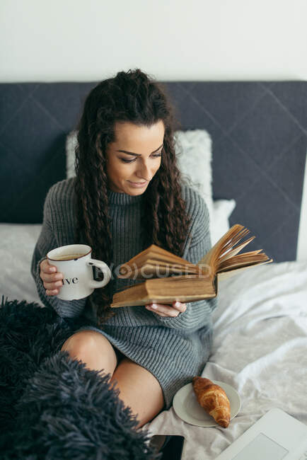 Mujer leyendo un libro con té en un sofá blanco. - foto de stock