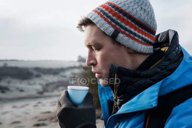 Homem soprando em café quente fazendo uma pausa enquanto caminhava na Inglaterra — Fotografia de Stock