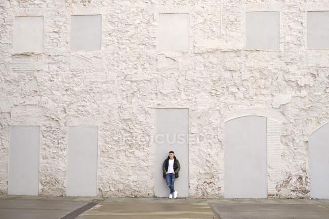 Junger Mann mit Händen an Taschen steht vor weißer Wand — Stockfoto