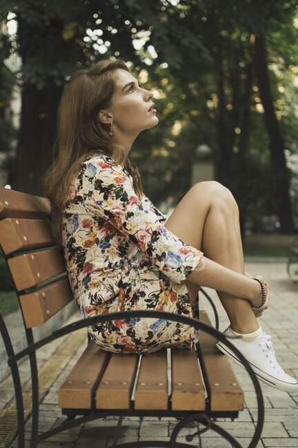 Крупный план молодой женщины в летнем платье, сидящей на скамейке — стоковое фото