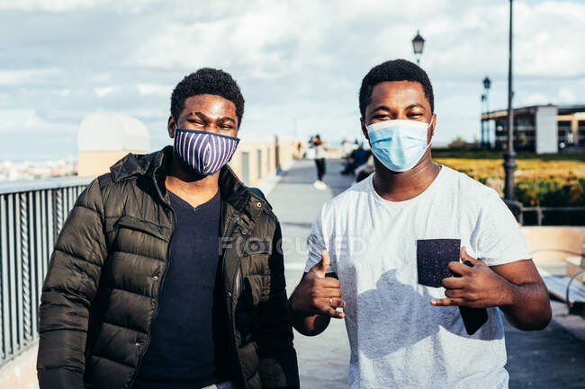 Portrait of two African-American friends with face masks posing happily on an urban space. — Stock Photo