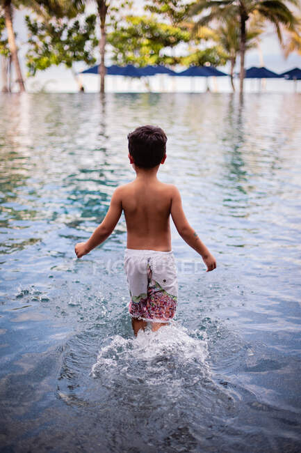 Garçon marchant dans une piscine à débordement dans un cadre tropical. — Photo de stock