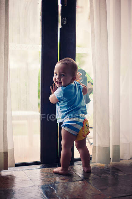 Little barefoot boy holding on to a big glass door. — Stock Photo