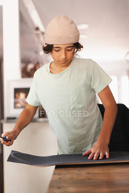 Écolier moyen garçon appliquant du ruban adhésif à sa planche à roulettes. — Photo de stock