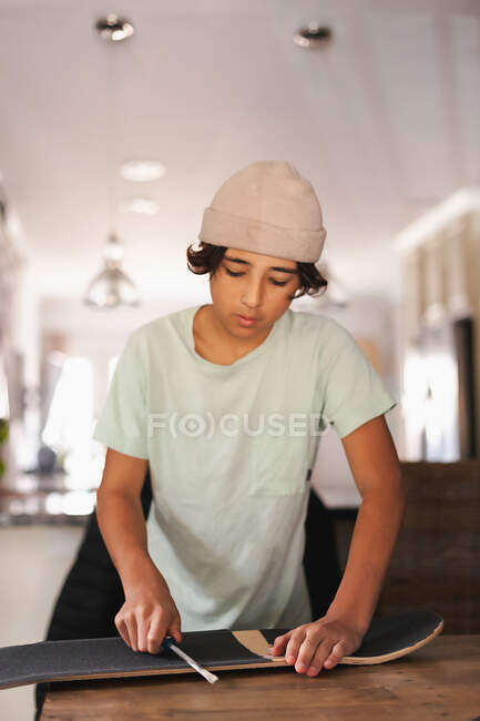 Niño de la escuela media aplicando cinta adhesiva a su monopatín. - foto de stock