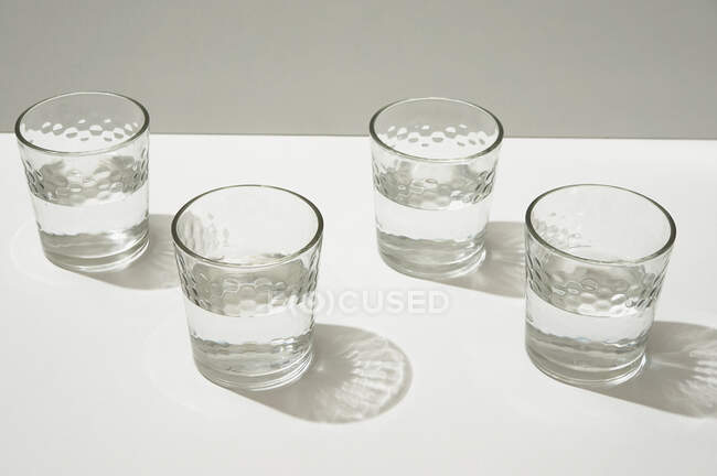 From above glasses with water casting shadows and sparkles on the white table. — Stock Photo