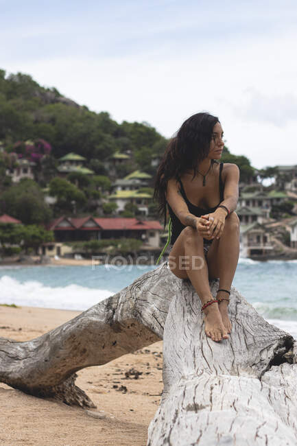 Eine junge Frau auf einem Baumstamm im Sand eines Inselstrandes — Stockfoto