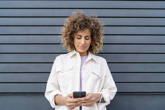 Красива жінка відправляє повідомлення зі свого смартфона на чорну стіну — стокове фото