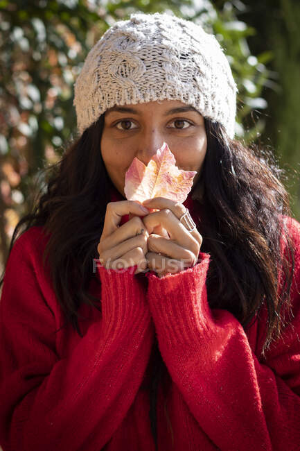 Beautiful young woman holding a leaf in autumn with a winter hat — Stock Photo