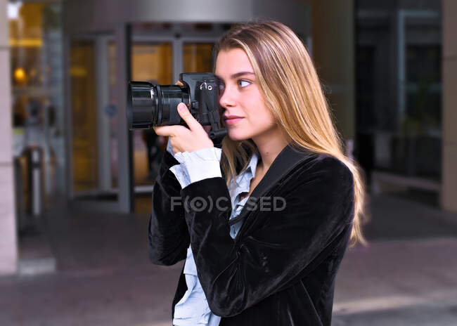 Atractiva joven espera con su cámara fotográfica delante de la puerta del hotel - foto de stock