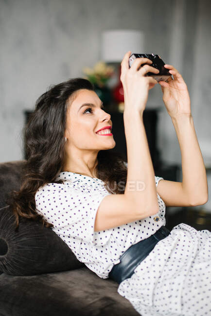 Mujer joven en vestido de estilo retro con cámara analógica haciendo una selfie - foto de stock