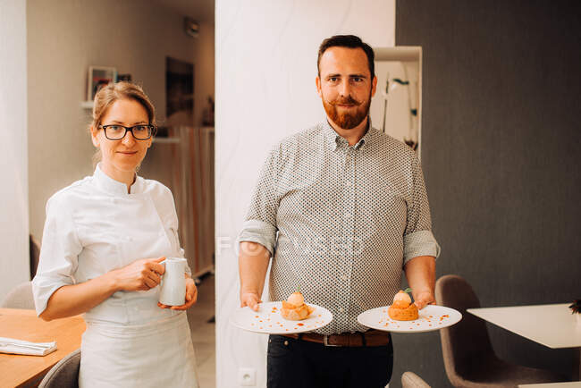 Couple of restaurant chefs holding plates with dessert — Stock Photo