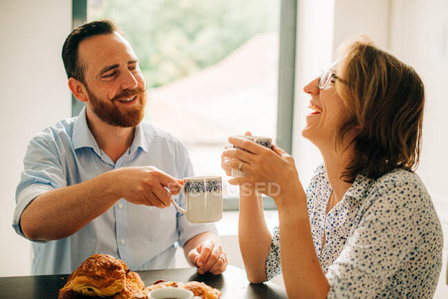 Casal sorrindo e rindo alegremente enquanto toma café da manhã — Fotografia de Stock