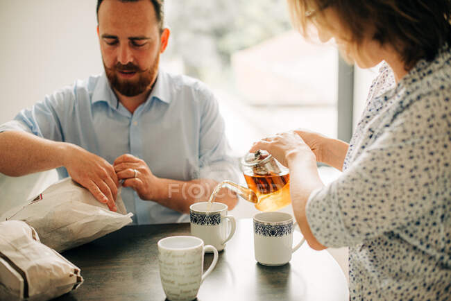 Couple having breakfast with tea. Man opening bags — Stock Photo
