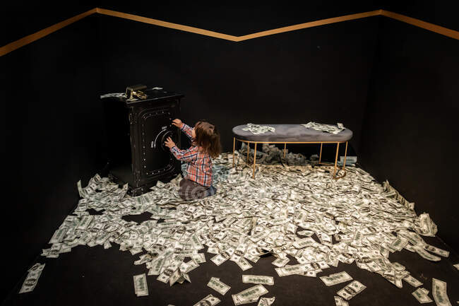 Маленькая девочка открывает сейф в окружении кучи денег би — стоковое фото