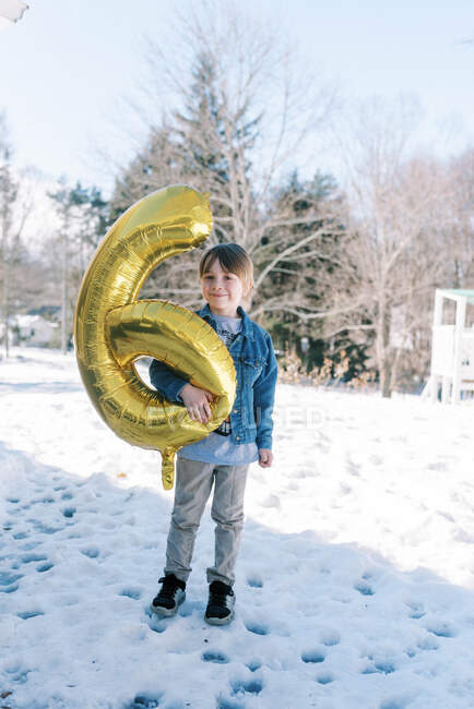 Kleiner Junge steht zum Geburtstag mit goldenem Luftballon im Schnee — Stockfoto