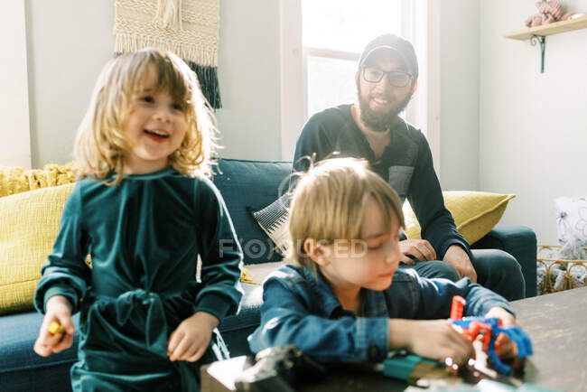 Un padre che guarda i suoi figli che giocano amorevolmente in una stanza soleggiata — Foto stock