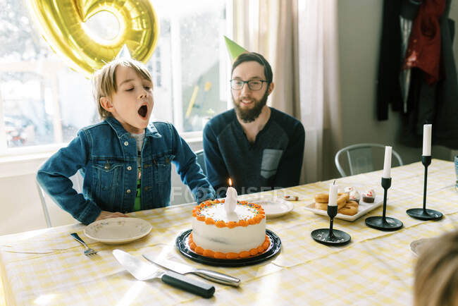 Pequeño niño soplando vela en su pastel de cumpleaños en la mesa con papá - foto de stock