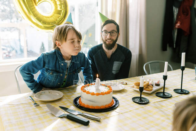 Little boy blowing out candle on his birthday cake at table with dad — Stock Photo