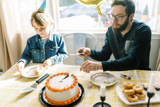 Padre e hijo cortando y sirviendo pastel de cumpleaños en celebración divertida - foto de stock