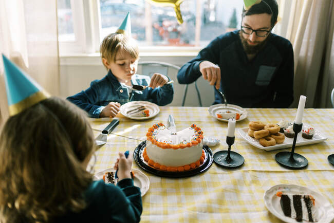 Una pequeña familia comiendo pastel de cumpleaños en la mesa y celebrando - foto de stock