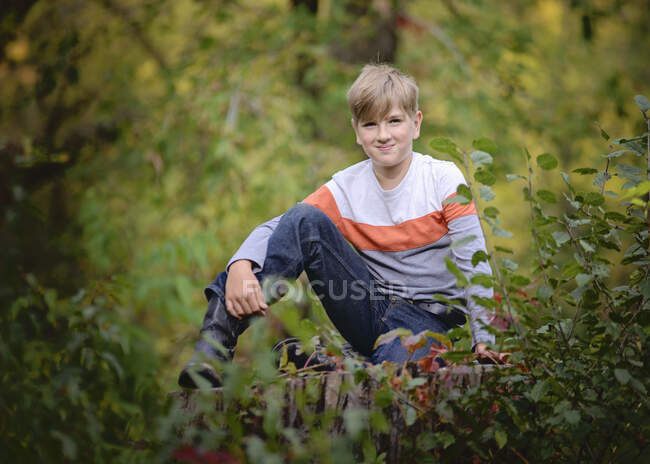 Junger blonder Junge sitzt draußen in den Bäumen — Stockfoto