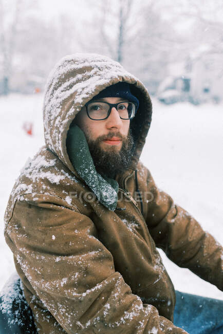 Улыбающийся молодой человек с бородой и очками в снежную бурю, вспахивающий диск — стоковое фото