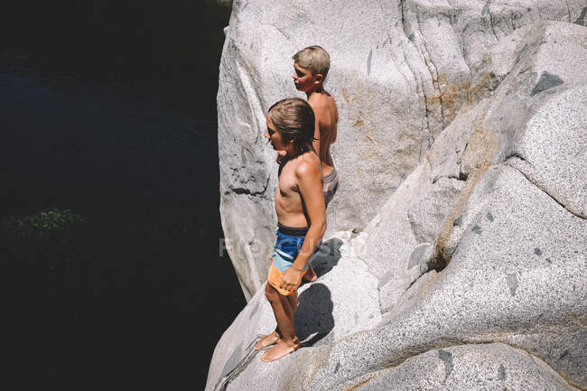Dos chicos se paran en un acantilado sobre el agua oscura - foto de stock