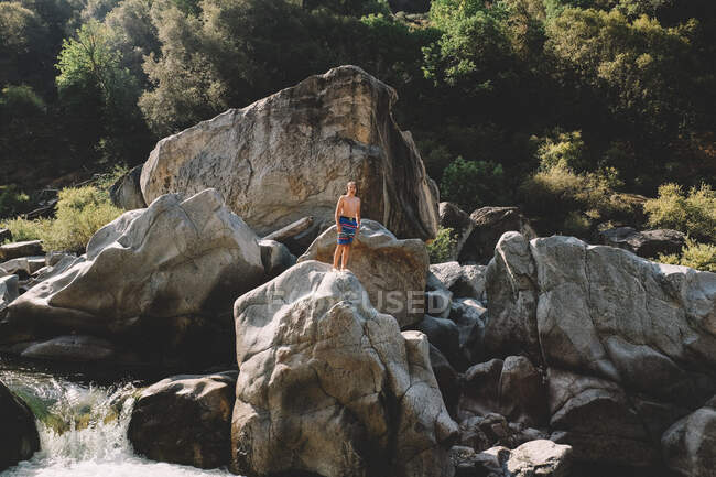 Joven niño se para en una roca sobre una cascada en verano - foto de stock